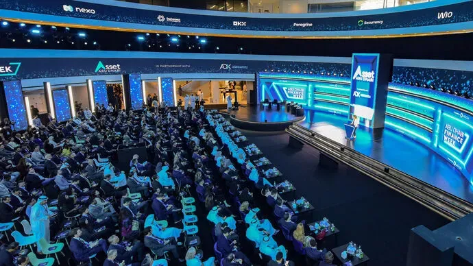 Abu Dhabi Finance Week conference event with a large audience seated in a modern venue, featuring a well-lit stage and digital displays.